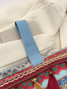 Dettaglio borsa boho con ricami geometrici, nastro intrecciato e nappe rosse vivaci