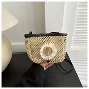 Close-up of woven straw bucket bag with large white daisy flower and black shoulder strap