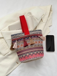 Dettaglio di borsa a secchiello boho intrecciata con nappe colorate e manico rosso