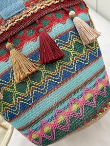 Dettaglio borsa a secchiello boho intrecciata con nappe colorate e motivi etnici a onde