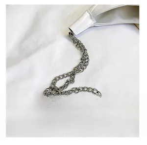 Détail d'une bandoulière en chaîne tissée argentée sur un sac cabas en cuir PU blanc