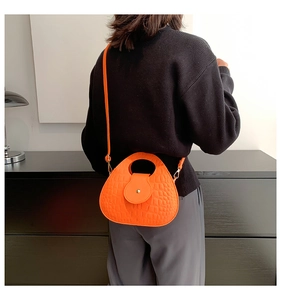 Détail du sac à main orange vif gaufré crocodile porté en bandoulière sur un modèle