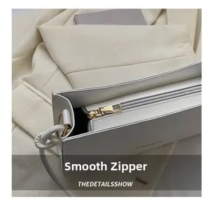Gros plan sur la fermeture dorée et le logo gaufré de ce sac blanc en cuir chic