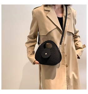 Sac à bandoulière noir effet crocodile avec fermoir doré porté par un mannequin