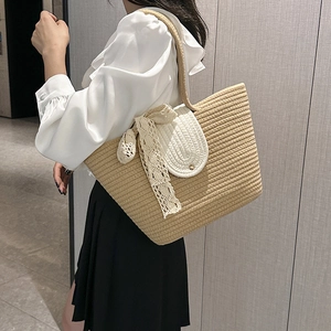 Minimalist khaki woven beach tote bag with white lace bow detail shown on a shoulder