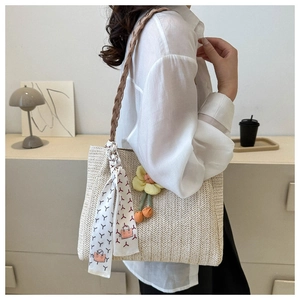 Detail of hand-woven straw shoulder bag with sunflower charm and decorative silk scarf