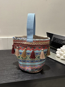 Dettaglio borsa a secchiello boho con motivi intrecciati colorati e nappe rosso scuro