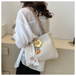 Detail of beige woven tote bag with yellow flower pendant and silk ribbon on shoulder