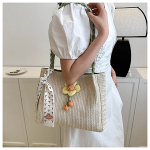 Detail of woven tote bag featuring a green handle, floral charm, and stylish silk scarf