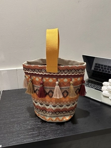 Dettaglio delle nappe colorate e della trama geometrica su una borsa a secchiello boho