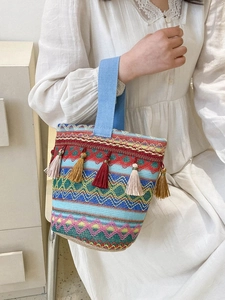 Dettaglio borsa a secchiello intrecciata multicolore con lunghe frange e manico in tessuto blu