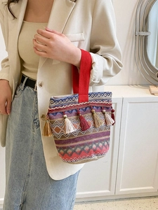 Dettaglio di borsa boho intrecciata con nappe colorate e ampi manici in tessuto rosso