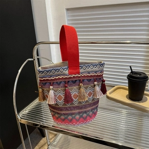 Dettaglio borsa etnica intrecciata con motivi geometrici e nappe decorative colorate