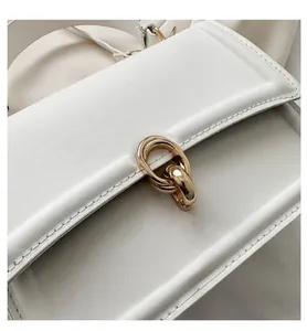 Detailed close-up of white leather handbag featuring a golden oval metal buckle