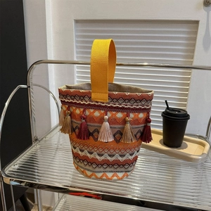 Dettaglio borsa a secchiello etnica intrecciata con motivi geometrici e nappe colorate
