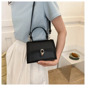 Detail of a matte black leather handbag with a gold buckle and adjustable strap