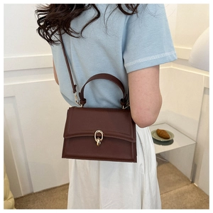 Detail of a dark brown crossbody bag with gold ring buckle and matte leather texture