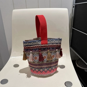 Dettaglio borsa a secchiello etnica intrecciata con motivi geometrici e nappe colorate