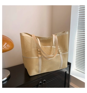 Close-up of a large beige mesh beach tote with reinforced straps on a wooden shelf