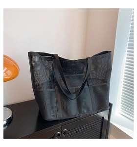 Detail of a black mesh beach tote bag with multiple pockets on a stylish dark wood surface