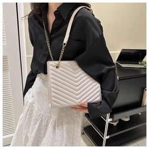 Close-up of a beige quilted shoulder bag with V-shaped stitching and chain strap