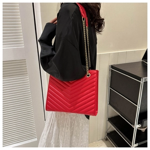 Detail of red quilted crossbody bag with V-shaped stitching and gold chain strap