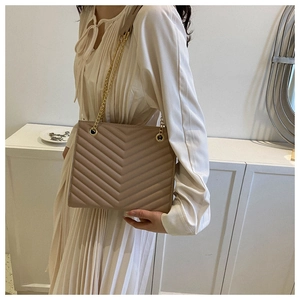 Detailed view of light brown V-quilted faux leather texture and gold chain strap detail