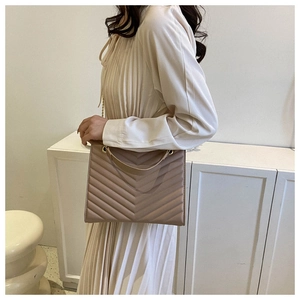 Detail of taupe quilted crossbody bag with V-shaped texture and metal chain strap