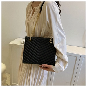 Detail of black chevron quilted leather shoulder bag with gold chain strap on model