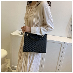 Detail of black quilted shoulder bag featuring gold chain strap and chevron stitching