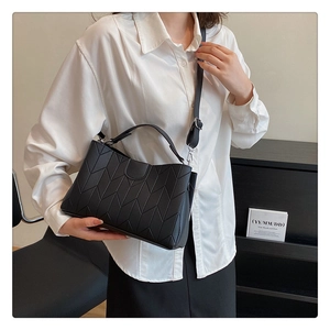 Detail of the black geometric V-quilted texture and silver hardware on a crossbody bag