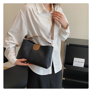 Detail of black quilted leather crossbody bag with brown straps on a model in white shirt