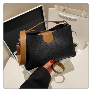 Detail of black quilted shoulder bag with contrast brown handle and V-pattern stitching