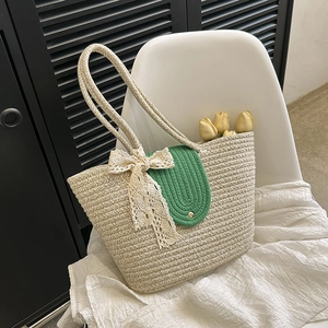 Detail of straw woven tote bag featuring a green flap and large white lace bow charm