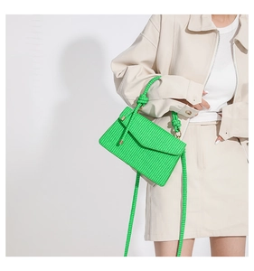 Detail of a bright green woven leather crossbody bag with a knot handle design