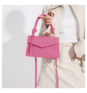 Model holding a bright pink woven crossbody bag with thick knot handle and metal ring detail