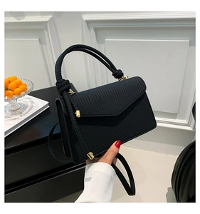 Detail of black woven texture handbag with thick knotted handle and gold metal hardware