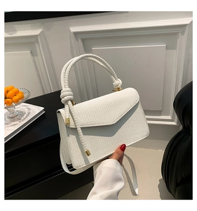 Detail of white woven texture handbag with knotted handle and elegant gold metal hardware