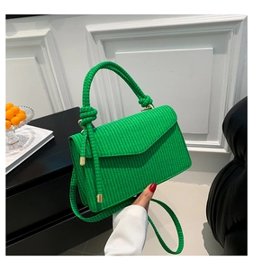 Close-up of bright green woven textured handbag with knot handle and golden hardware