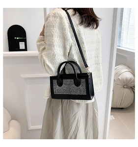 Détail d'un sac bandoulière noir avec clous argentés porté dans un décor d'intérieur chic