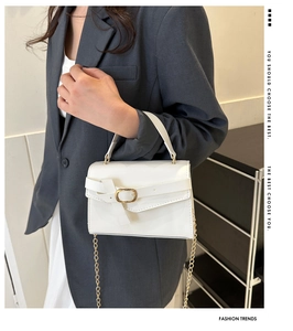 Detailed view of a white leather handbag with gold chain strap and buckle on a model