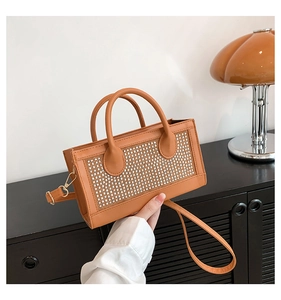 Détail du sac à main orange à strass montrant des cristaux brillants et deux poignées