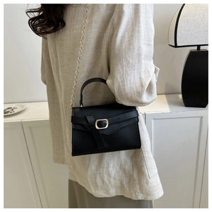 Close-up of stylish black square handbag with gold chain strap worn by a model
