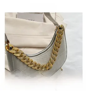 Detalle de bolso medialuna blanco con grabado de cocodrilo y cadena dorada decorativa