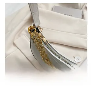 Detalle del bolso de hombro blanco con patrón de cocodrilo, cadena dorada y cremallera