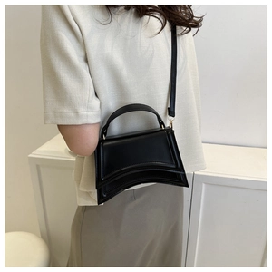 Sac à main noir minimaliste avec base incurvée porté par un mannequin en studio