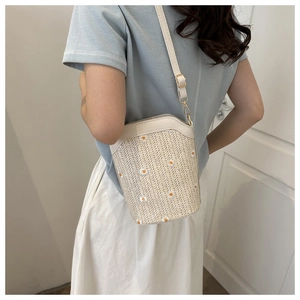 Detailed view of cream woven bucket bag featuring delicate daisy flower embroidery and strap