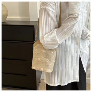 Détail du sac seau en paille beige avec broderie de marguerites et fine bandoulière