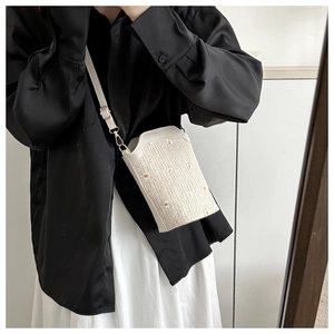 Détail d'un sac seau en paille tissée beige avec broderie marguerite et bandoulière cuir