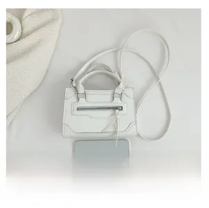 Mini white leather handbag size comparison next to a smartphone on white fabric
